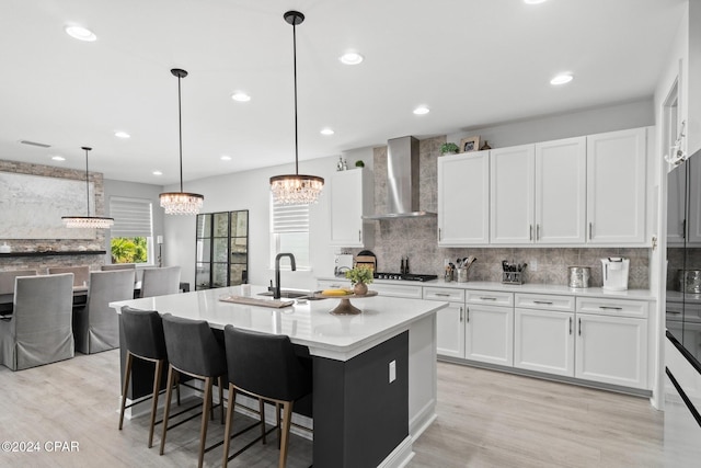 kitchen with pendant lighting, white cabinetry, wall chimney range hood, and a kitchen island with sink