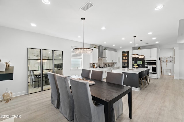 dining area featuring light wood-type flooring, an inviting chandelier, and sink