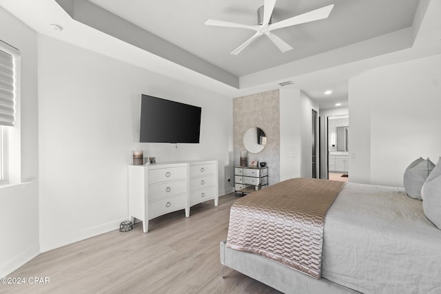 bedroom featuring connected bathroom, a tray ceiling, light hardwood / wood-style flooring, and ceiling fan