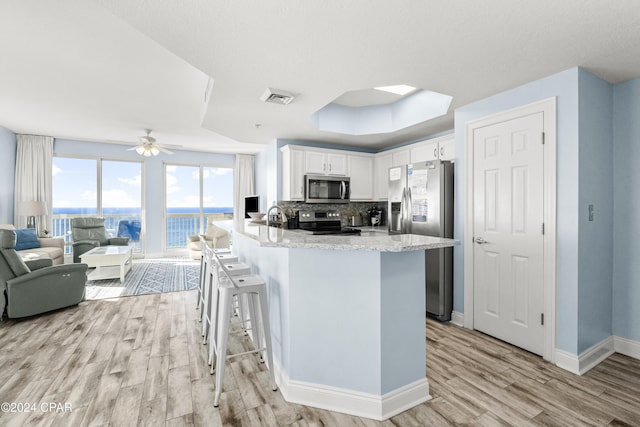 kitchen featuring backsplash, a kitchen breakfast bar, a raised ceiling, white cabinetry, and stainless steel appliances