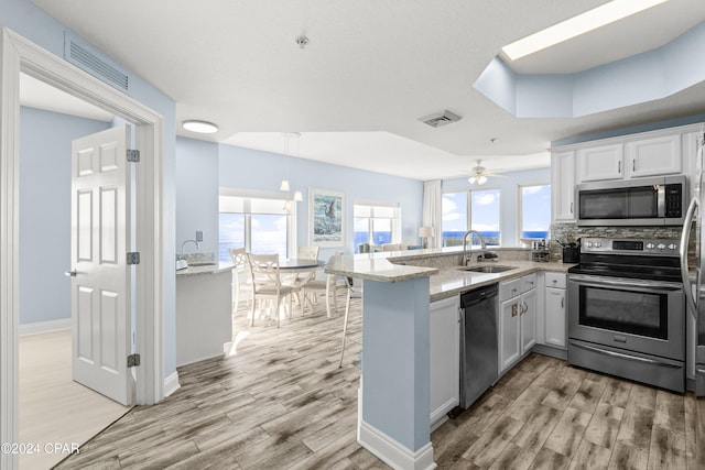 kitchen featuring kitchen peninsula, light wood-type flooring, stainless steel appliances, sink, and white cabinetry