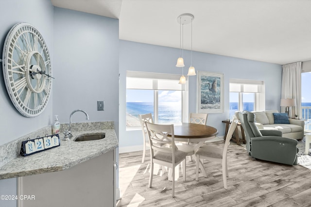 dining space with plenty of natural light, a water view, light wood-type flooring, and sink