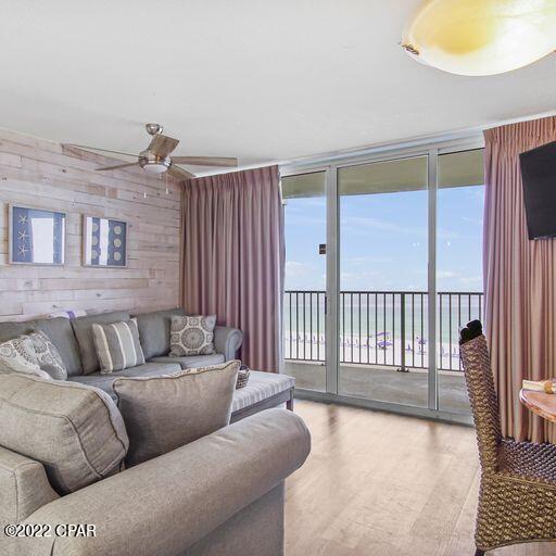 living room featuring light hardwood / wood-style flooring, expansive windows, ceiling fan, and wood walls