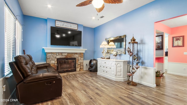 living area with a stone fireplace, a wealth of natural light, ceiling fan, and wood-type flooring