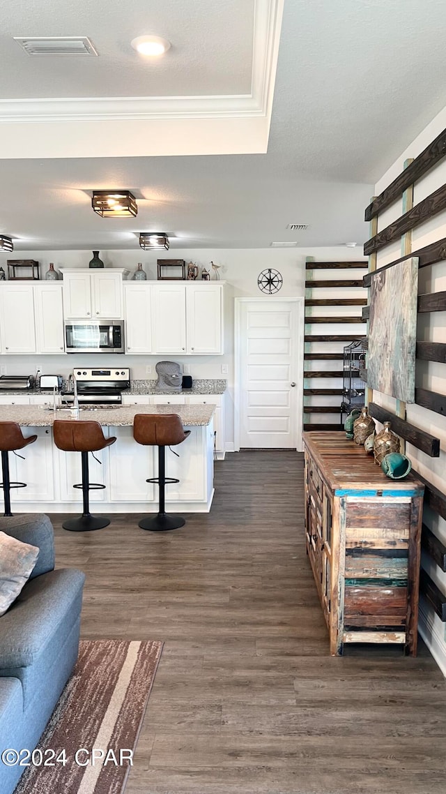 kitchen with a kitchen bar, white cabinetry, light stone countertops, and dark wood-type flooring