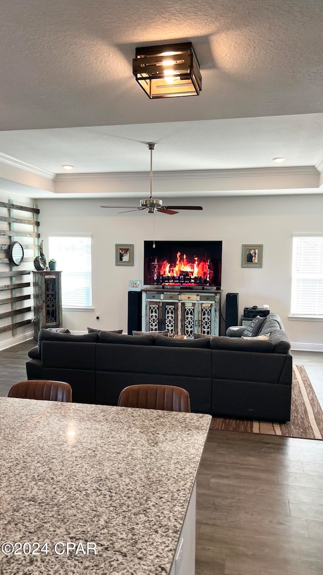 living room featuring ornamental molding, a textured ceiling, a tray ceiling, ceiling fan, and dark wood-type flooring