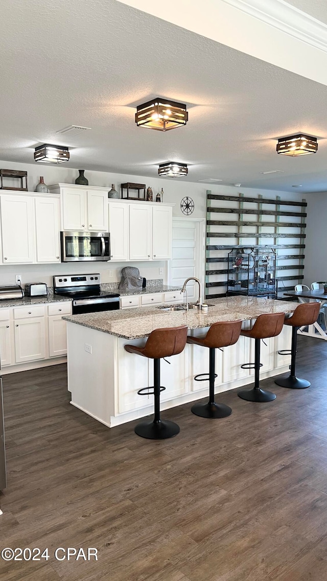 kitchen featuring light stone counters, a breakfast bar, stainless steel appliances, a kitchen island with sink, and white cabinets