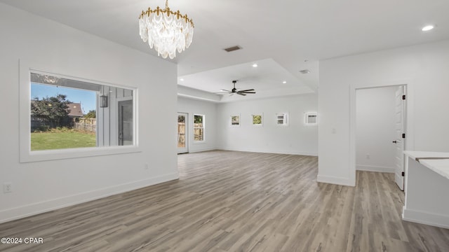 unfurnished living room with ceiling fan with notable chandelier, light wood-type flooring, and a tray ceiling