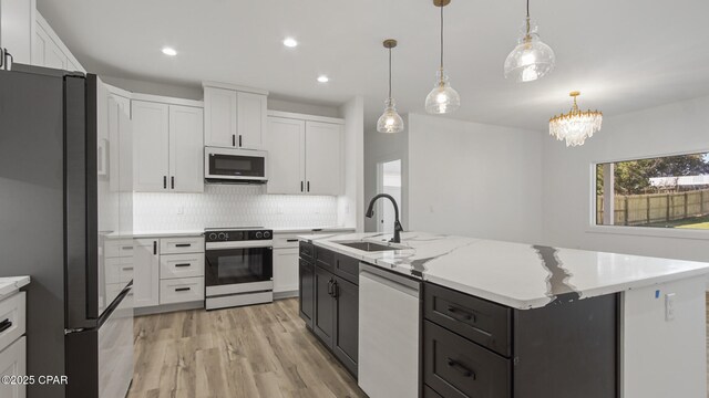 kitchen featuring pendant lighting, dishwasher, stove, a kitchen island with sink, and refrigerator