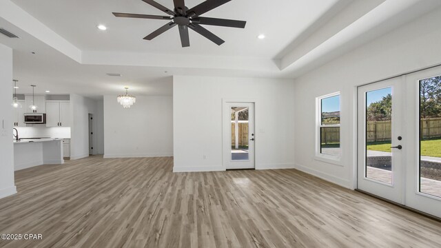 unfurnished living room with a raised ceiling, french doors, and light hardwood / wood-style flooring