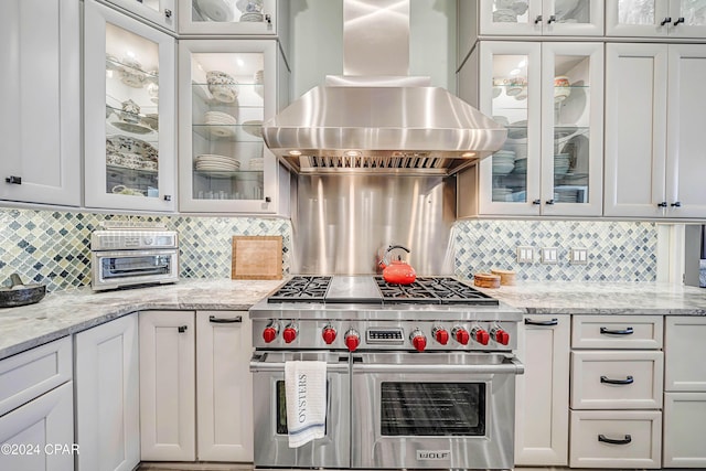 kitchen with island range hood, light stone countertops, white cabinets, and range with two ovens