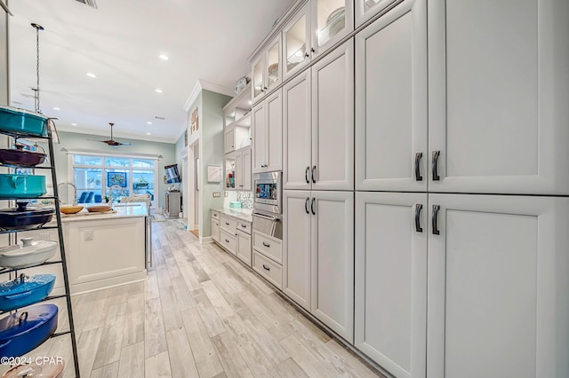 kitchen featuring ceiling fan, white cabinetry, stainless steel microwave, ornamental molding, and light hardwood / wood-style floors