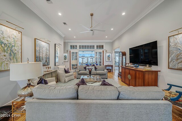 living room featuring decorative columns, ceiling fan with notable chandelier, crown molding, and light hardwood / wood-style flooring