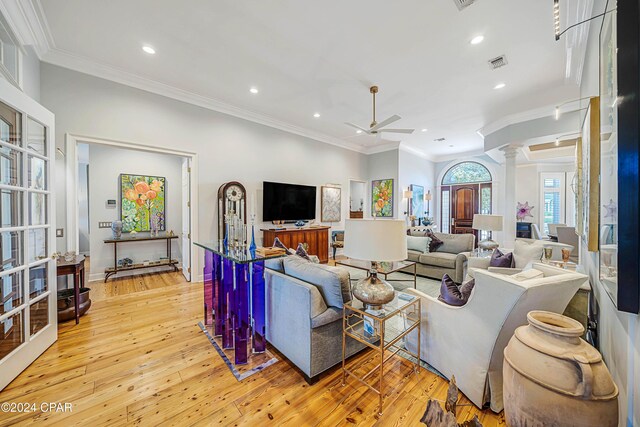 living room with crown molding, light hardwood / wood-style flooring, ceiling fan with notable chandelier, and ornate columns