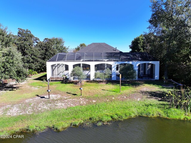 back of house featuring glass enclosure, a water view, and a yard