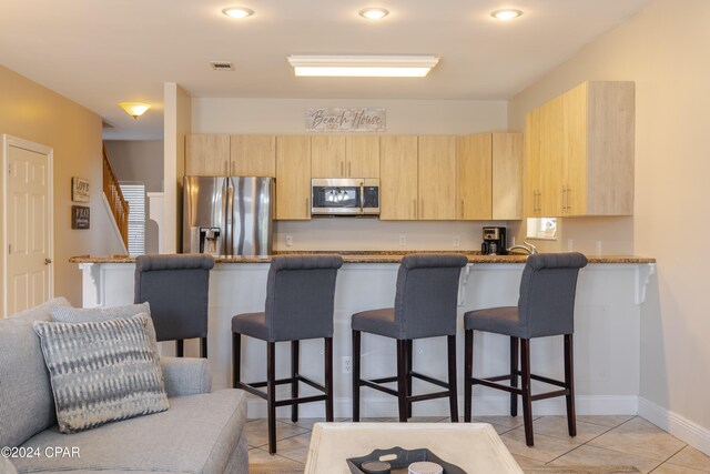 kitchen with kitchen peninsula, light brown cabinets, stainless steel appliances, and a breakfast bar