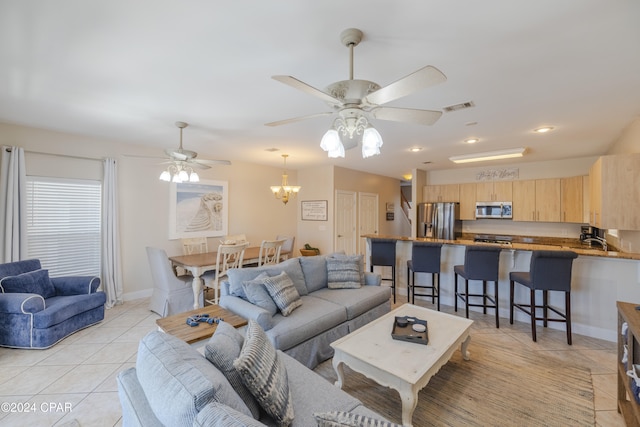 living room featuring sink, light tile patterned floors, and ceiling fan with notable chandelier