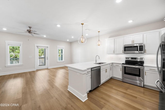 kitchen featuring pendant lighting, white cabinets, appliances with stainless steel finishes, light hardwood / wood-style floors, and kitchen peninsula