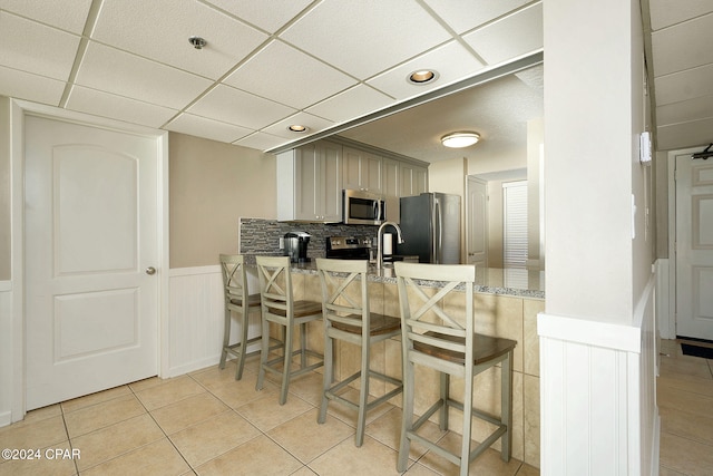 kitchen featuring a drop ceiling, stainless steel appliances, tasteful backsplash, a breakfast bar area, and light tile patterned floors