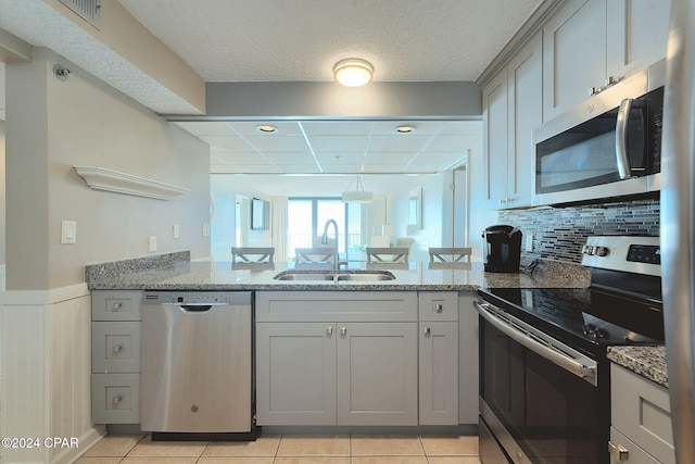 kitchen featuring appliances with stainless steel finishes, light tile patterned floors, light stone counters, and sink