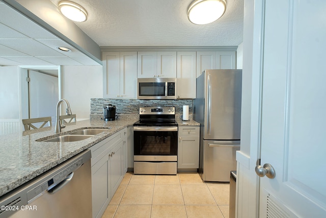 kitchen with light stone countertops, decorative backsplash, stainless steel appliances, sink, and light tile patterned floors