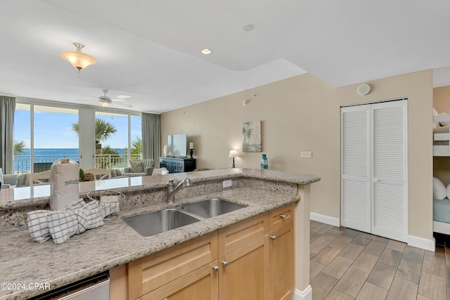 kitchen with light brown cabinetry, dishwasher, sink, ceiling fan, and light stone counters