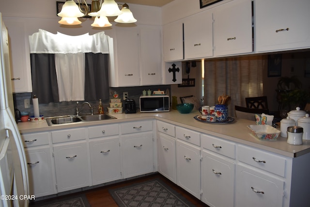 kitchen featuring backsplash, sink, white cabinets, and a notable chandelier