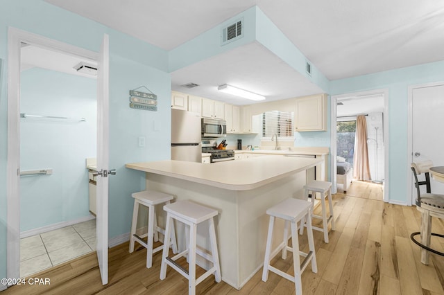 kitchen with a kitchen breakfast bar, white cabinetry, light hardwood / wood-style flooring, and appliances with stainless steel finishes