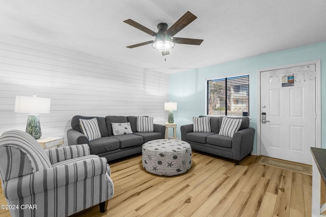 living room featuring ceiling fan, wood walls, and light hardwood / wood-style flooring