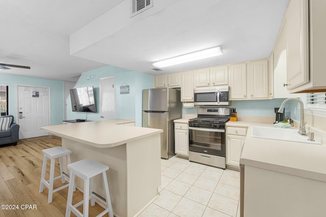 kitchen featuring a breakfast bar, stainless steel appliances, ceiling fan, sink, and light hardwood / wood-style floors