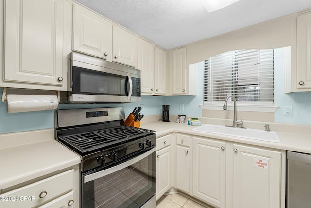 kitchen featuring appliances with stainless steel finishes, a textured ceiling, sink, light tile patterned floors, and white cabinets