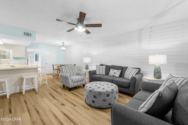 living room with ceiling fan with notable chandelier and light hardwood / wood-style flooring