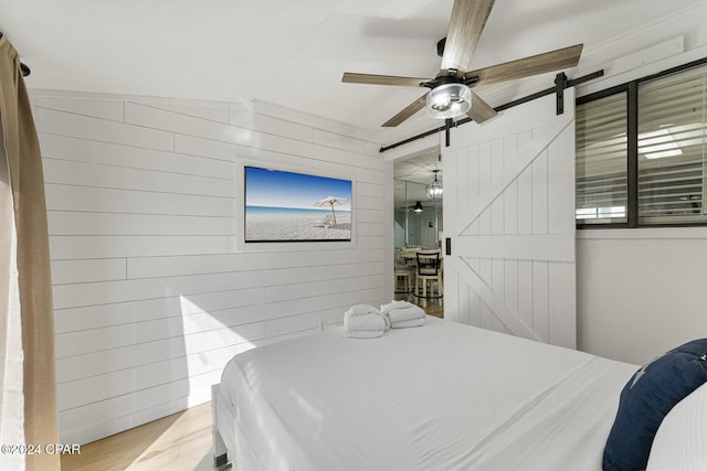 bedroom featuring wood walls, ceiling fan, and a barn door