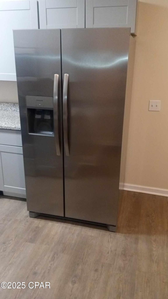 interior space with stainless steel fridge, light stone countertops, and light hardwood / wood-style floors