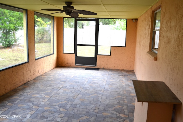 unfurnished sunroom with a healthy amount of sunlight, a paneled ceiling, and ceiling fan