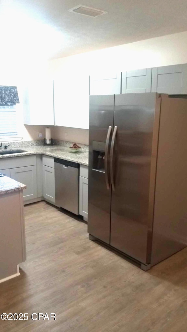 kitchen featuring white cabinetry, sink, light wood-type flooring, and appliances with stainless steel finishes