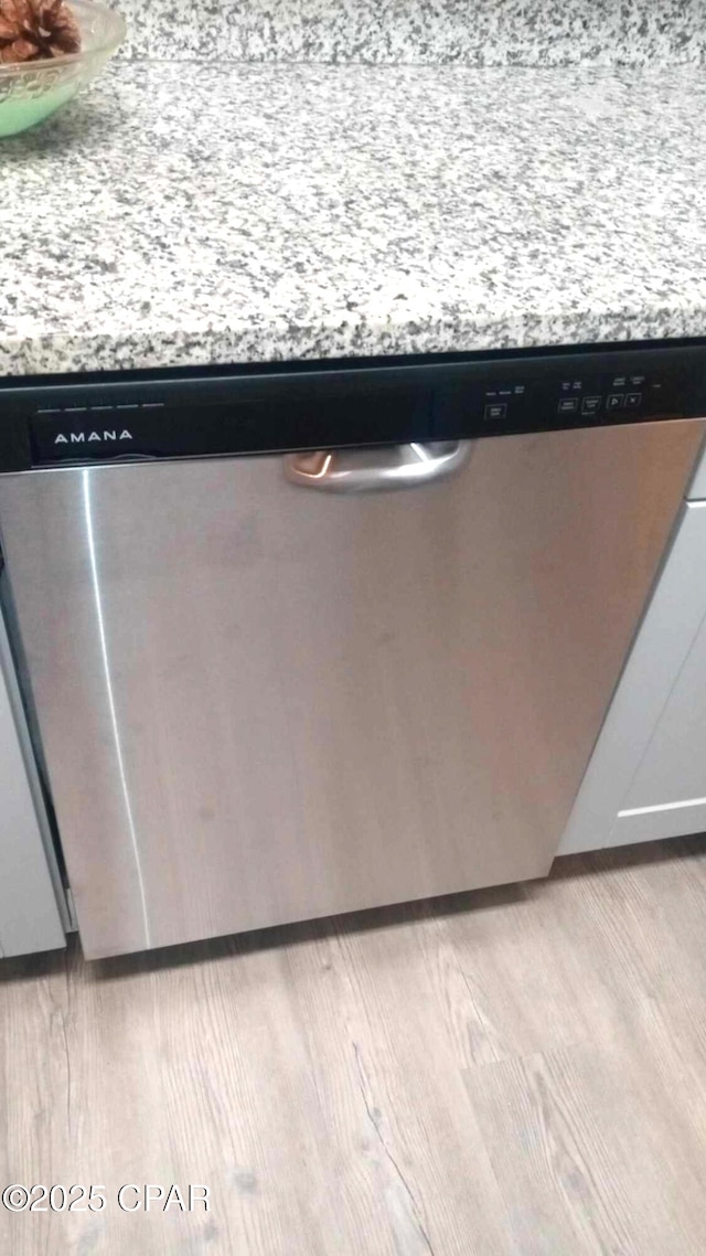 room details with stainless steel dishwasher, light stone countertops, and light hardwood / wood-style floors