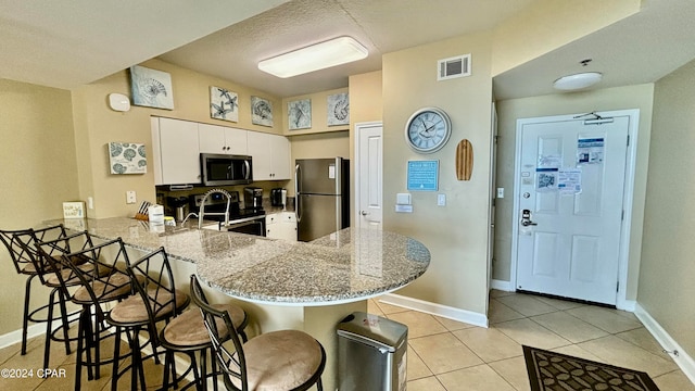 kitchen featuring white cabinetry, kitchen peninsula, a breakfast bar, light tile patterned floors, and appliances with stainless steel finishes