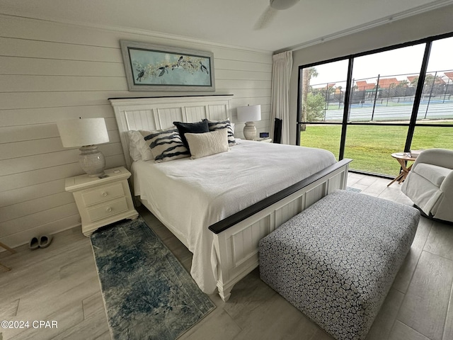 bedroom with ceiling fan, crown molding, light hardwood / wood-style floors, and wooden walls