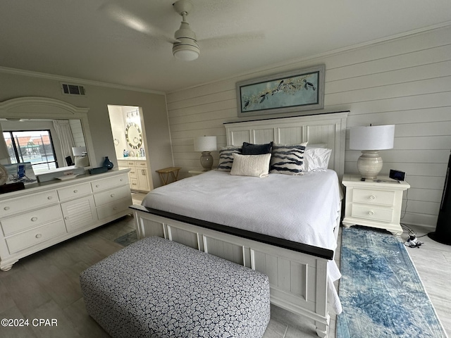 bedroom featuring ensuite bathroom, wood walls, dark hardwood / wood-style flooring, ornamental molding, and ceiling fan