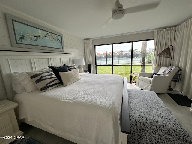 bedroom with wood walls, light hardwood / wood-style floors, crown molding, ceiling fan, and a water view