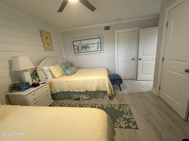 bedroom featuring ceiling fan, light hardwood / wood-style floors, ornamental molding, and wood walls