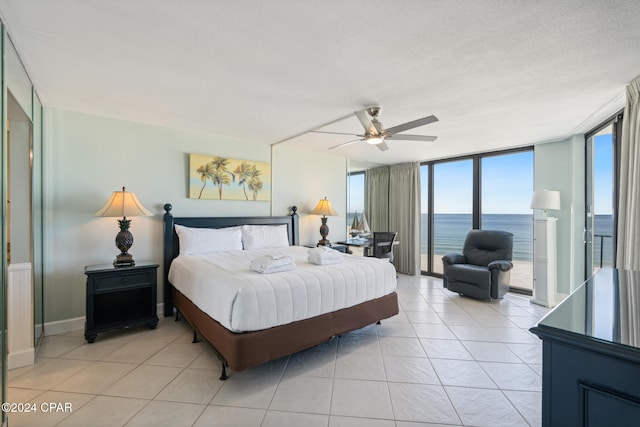 bedroom featuring floor to ceiling windows, a textured ceiling, ceiling fan, light tile patterned floors, and a water view