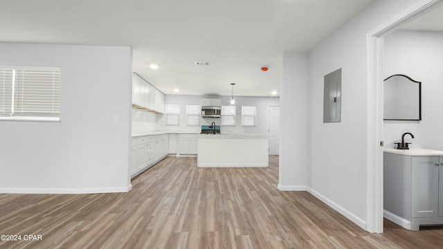 kitchen with sink, hanging light fixtures, electric panel, light hardwood / wood-style floors, and white cabinets