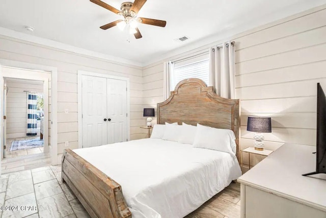 bedroom featuring ceiling fan, a closet, wood walls, and light hardwood / wood-style flooring