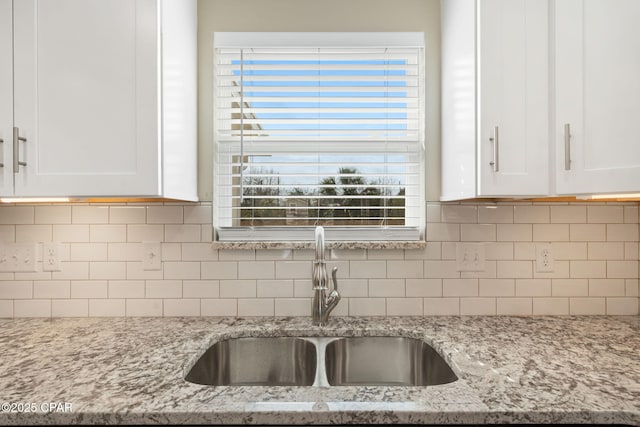 kitchen featuring light stone counters, white cabinetry, sink, and tasteful backsplash