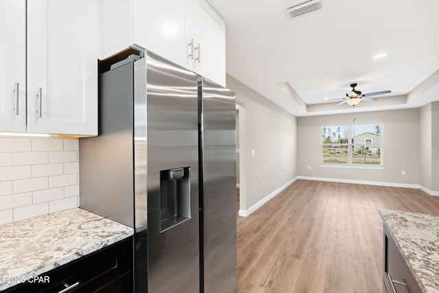 kitchen with light stone counters, tasteful backsplash, stainless steel fridge, a raised ceiling, and white cabinets