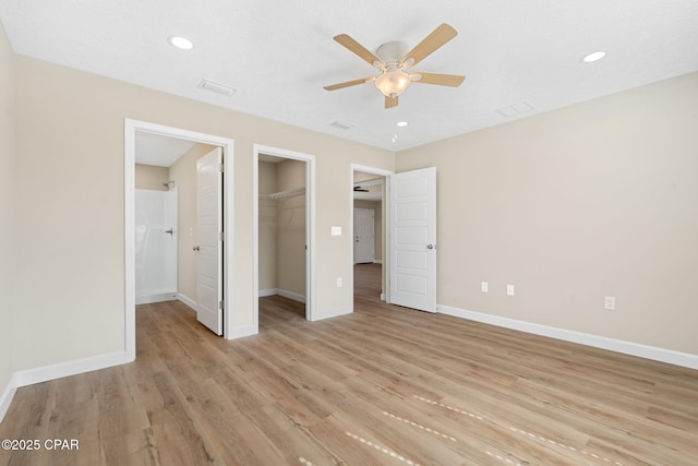 unfurnished bedroom featuring ceiling fan, a spacious closet, light hardwood / wood-style floors, and a closet