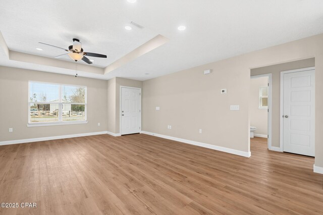 unfurnished living room featuring a raised ceiling, ceiling fan, and light wood-type flooring