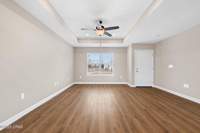 empty room with ceiling fan, a raised ceiling, and hardwood / wood-style floors